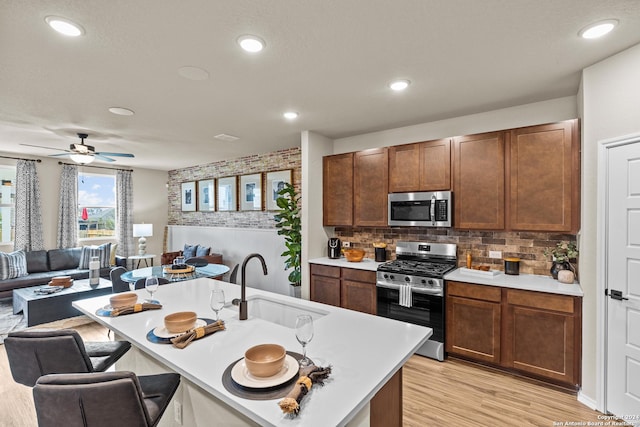 kitchen featuring sink, light hardwood / wood-style flooring, stainless steel appliances, a center island with sink, and decorative backsplash