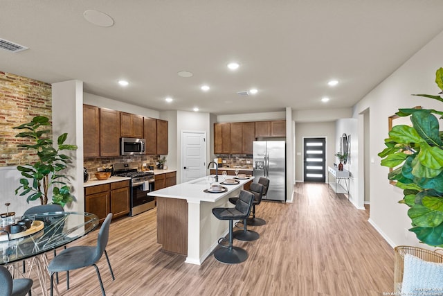 kitchen with appliances with stainless steel finishes, a breakfast bar, a center island with sink, and light wood-type flooring