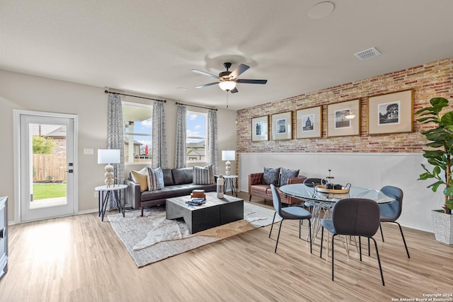 living room featuring ceiling fan, brick wall, a healthy amount of sunlight, and light wood-type flooring