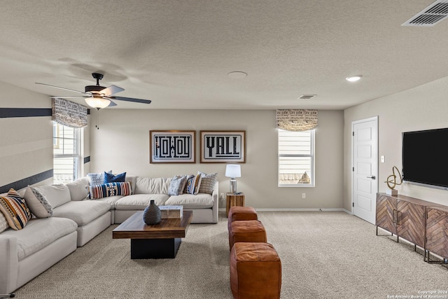 living room with a textured ceiling, light colored carpet, and ceiling fan