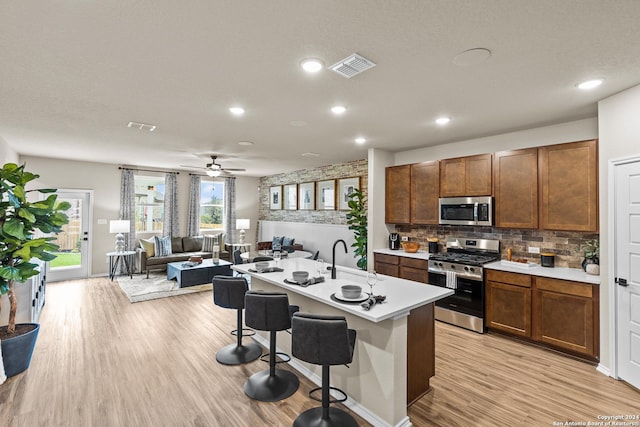 kitchen with sink, a kitchen breakfast bar, stainless steel appliances, a kitchen island with sink, and backsplash