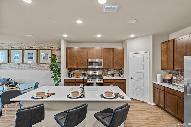 kitchen featuring a center island with sink, stainless steel appliances, light hardwood / wood-style floors, a kitchen bar, and decorative backsplash