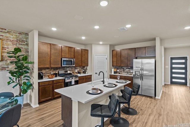 kitchen featuring sink, appliances with stainless steel finishes, a kitchen island with sink, light hardwood / wood-style floors, and a kitchen bar