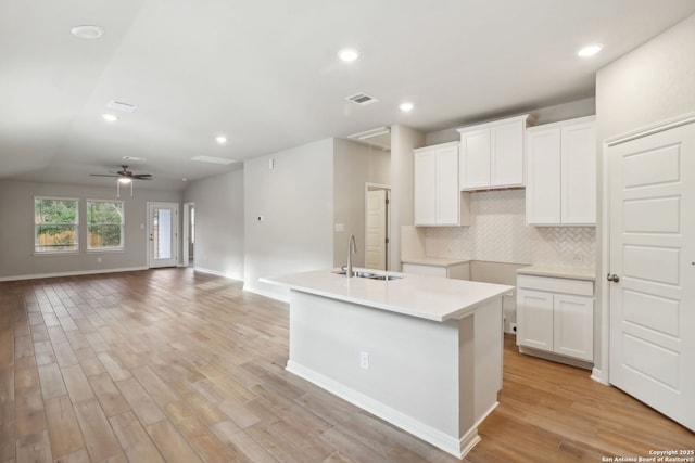 kitchen featuring sink, backsplash, white cabinets, a center island with sink, and light wood-type flooring