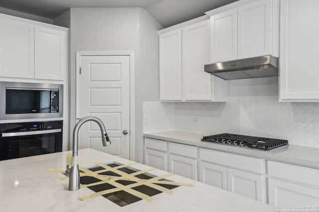 kitchen with stainless steel appliances, under cabinet range hood, decorative backsplash, white cabinetry, and light stone counters
