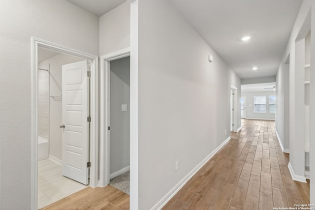 hall featuring light wood-style flooring, baseboards, and recessed lighting