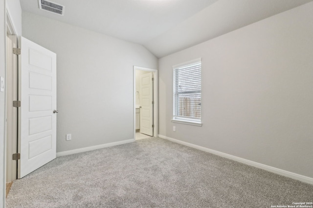 empty room featuring light colored carpet, vaulted ceiling, and baseboards