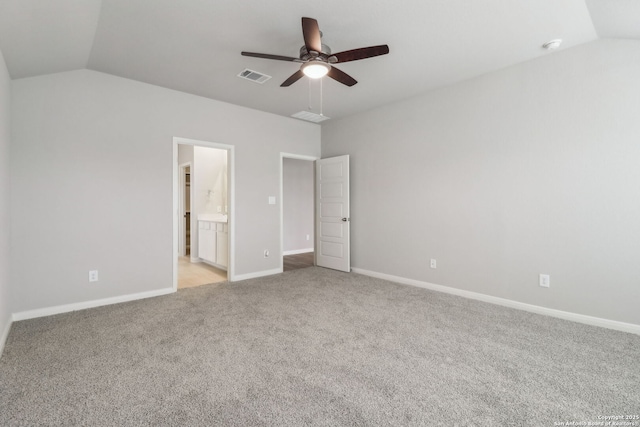 unfurnished bedroom featuring lofted ceiling, light carpet, baseboards, ensuite bathroom, and a ceiling fan
