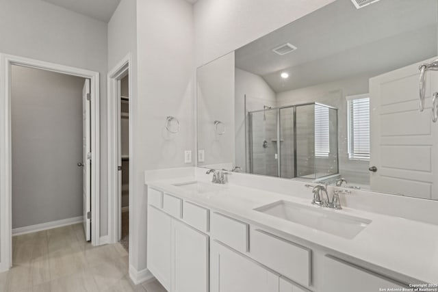 bathroom with a stall shower, double vanity, a spacious closet, and baseboards