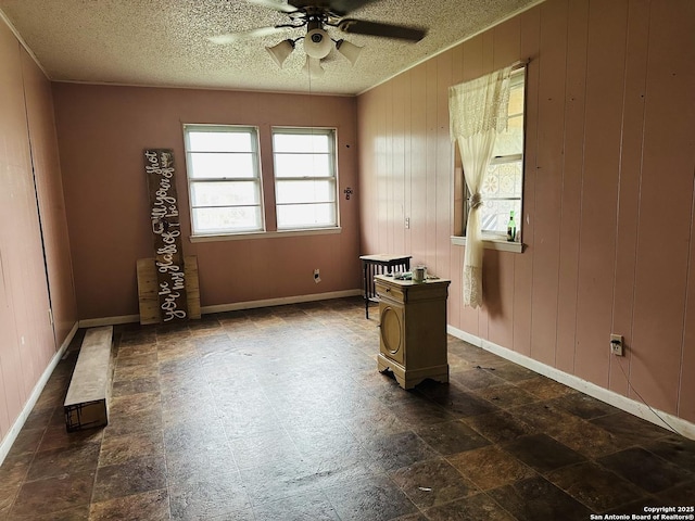 empty room featuring ceiling fan, wooden walls, and a textured ceiling