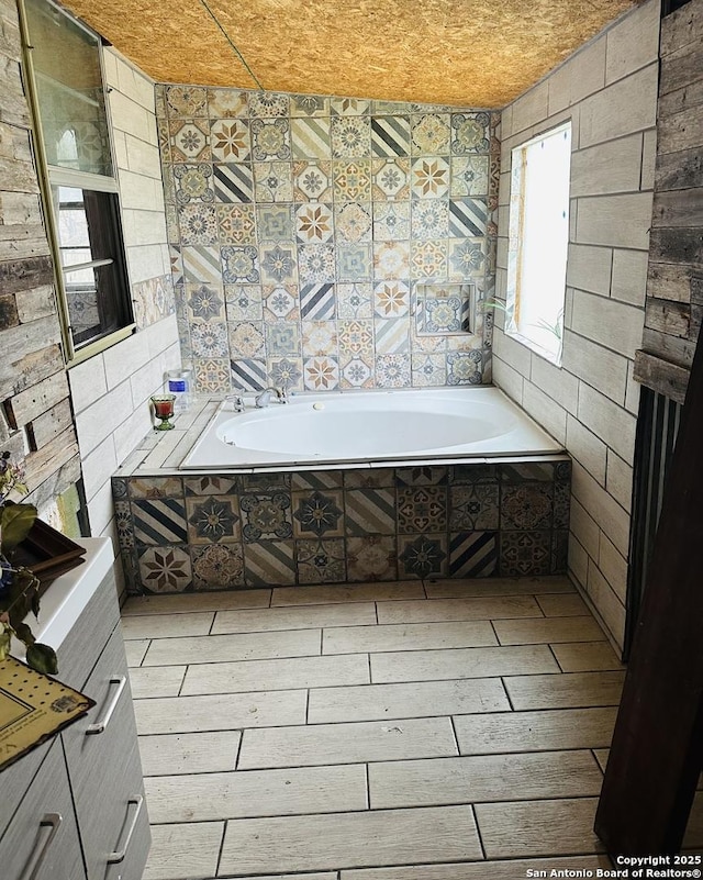 bathroom with tile walls, tiled tub, and hardwood / wood-style flooring