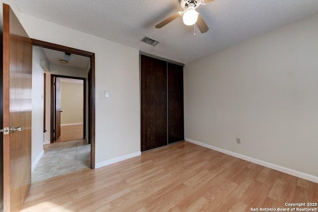 unfurnished bedroom featuring light wood-type flooring, a closet, a textured ceiling, and ceiling fan