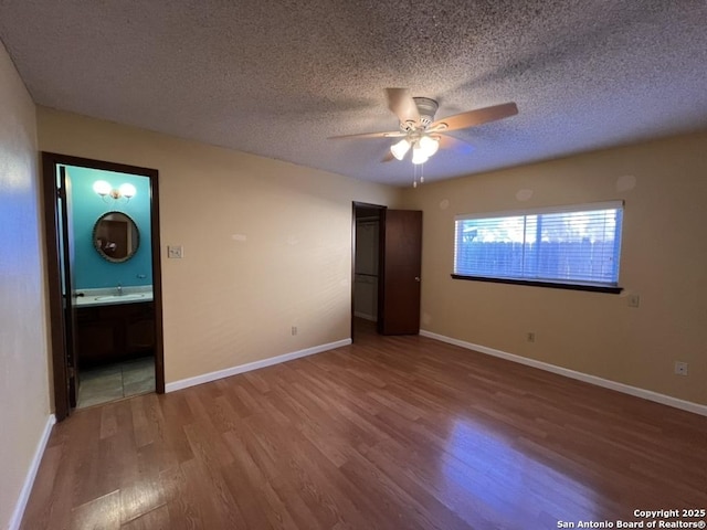 unfurnished bedroom with ceiling fan, hardwood / wood-style flooring, connected bathroom, and a textured ceiling