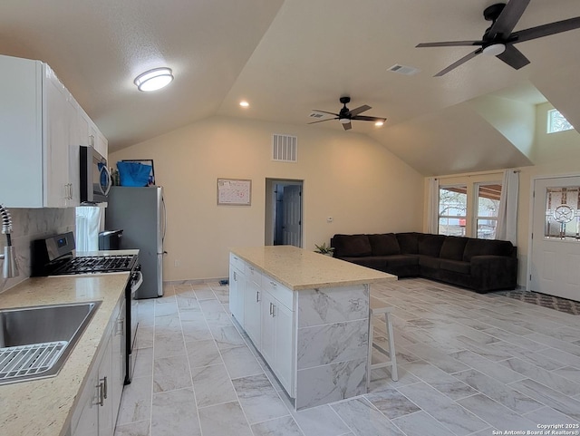 kitchen with lofted ceiling, appliances with stainless steel finishes, light stone countertops, white cabinets, and a kitchen island