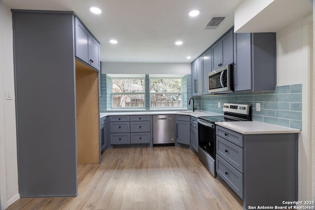 kitchen featuring tasteful backsplash, sink, light hardwood / wood-style flooring, and appliances with stainless steel finishes