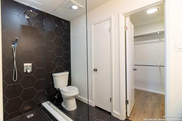 bathroom featuring wood-type flooring, toilet, and tiled shower