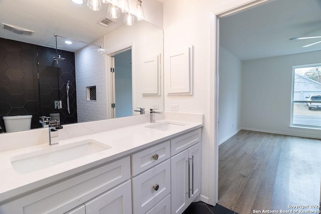 bathroom featuring ceiling fan, tiled shower, vanity, wood-type flooring, and toilet