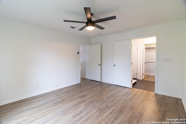 unfurnished bedroom with ceiling fan, a spacious closet, light hardwood / wood-style floors, and a closet