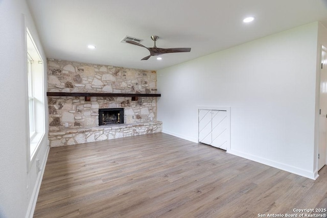 unfurnished living room with a stone fireplace, wood-type flooring, ceiling fan, and a wealth of natural light