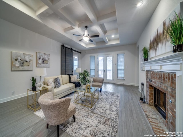 living room featuring coffered ceiling, a barn door, wood-type flooring, ceiling fan, and a fireplace