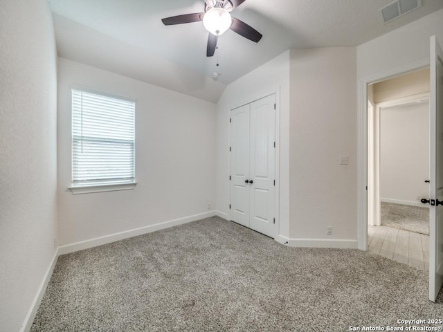 unfurnished bedroom featuring light carpet, vaulted ceiling, a closet, and ceiling fan