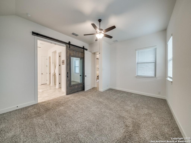 carpeted empty room with a barn door, lofted ceiling, and ceiling fan