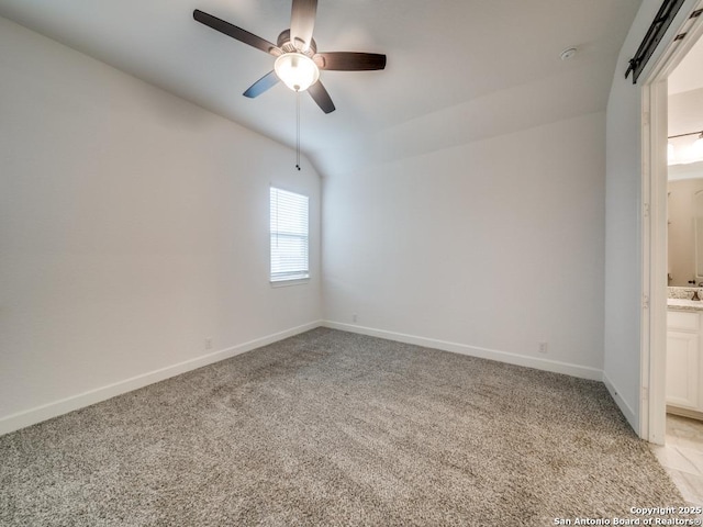 spare room with ceiling fan, lofted ceiling, a barn door, and light carpet