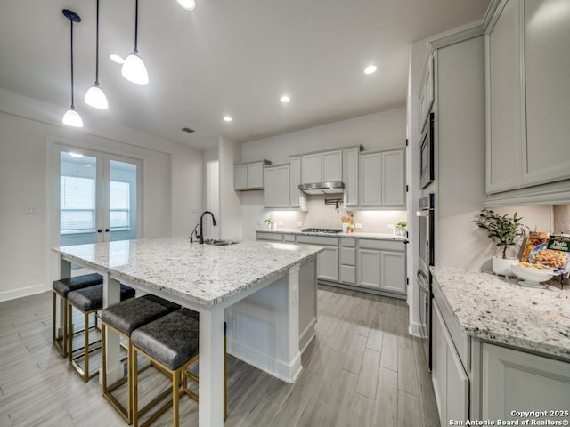 kitchen with sink, light stone counters, decorative light fixtures, appliances with stainless steel finishes, and a kitchen island with sink