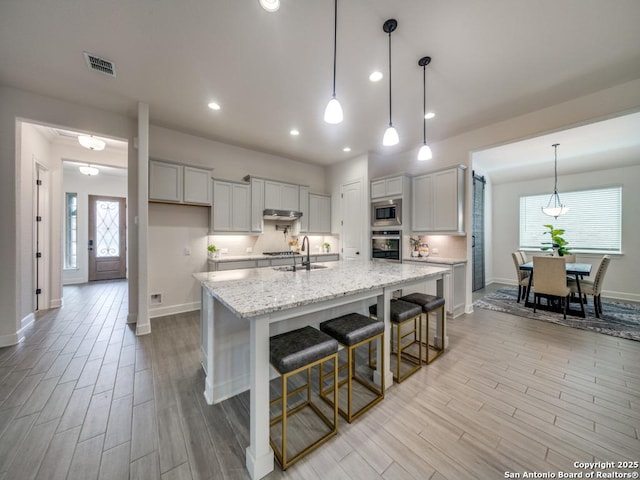 kitchen with appliances with stainless steel finishes, a breakfast bar, white cabinetry, light stone counters, and a center island with sink