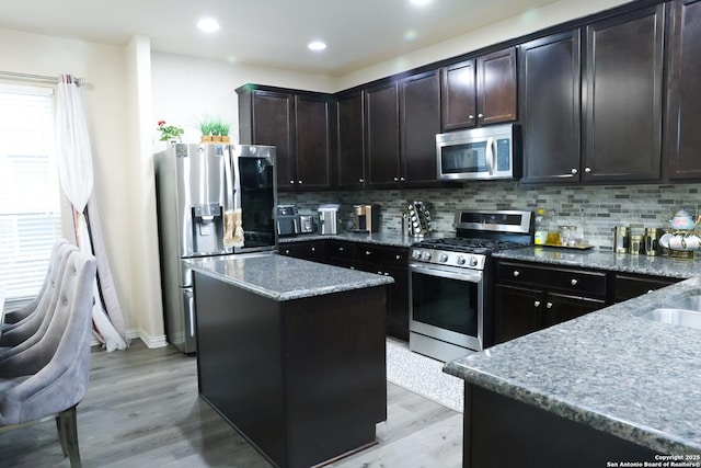 kitchen featuring stone countertops, a kitchen island, stainless steel appliances, light wood-style floors, and backsplash