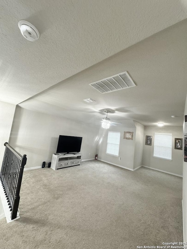 unfurnished living room featuring ceiling fan, light colored carpet, plenty of natural light, and a textured ceiling