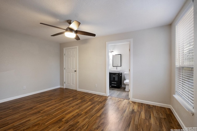 unfurnished bedroom featuring baseboards, dark wood finished floors, a ceiling fan, connected bathroom, and a sink