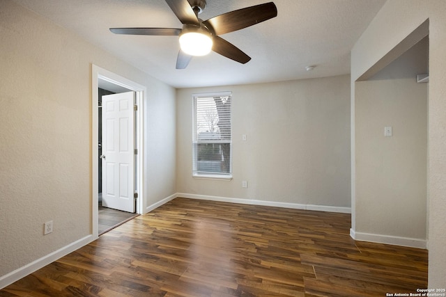 spare room featuring dark wood-style flooring, ceiling fan, and baseboards