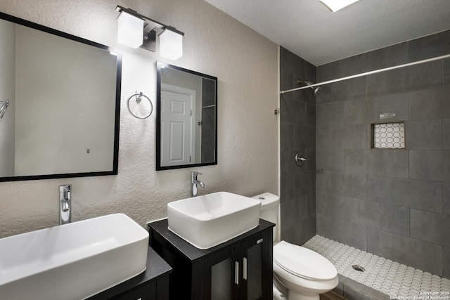 bathroom featuring toilet, two vanities, a textured wall, and a sink