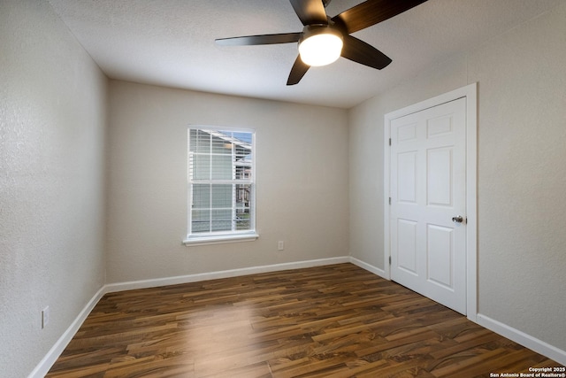 spare room featuring dark wood-style flooring, a textured wall, and baseboards