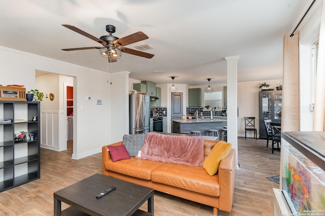 living room featuring ornate columns, crown molding, ceiling fan, and light wood-type flooring