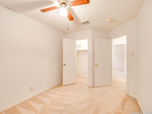 unfurnished bedroom with ceiling fan, light colored carpet, a textured ceiling, and a walk in closet