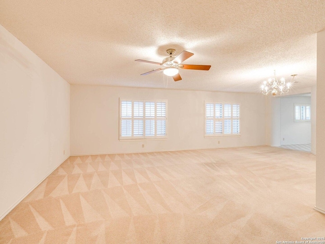 carpeted spare room with plenty of natural light, ceiling fan with notable chandelier, and a textured ceiling