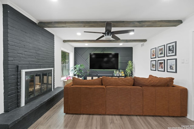 living room featuring a brick fireplace, beam ceiling, hardwood / wood-style floors, and ceiling fan