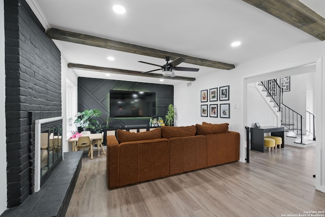 living room with a brick fireplace, wood-type flooring, beamed ceiling, and ceiling fan