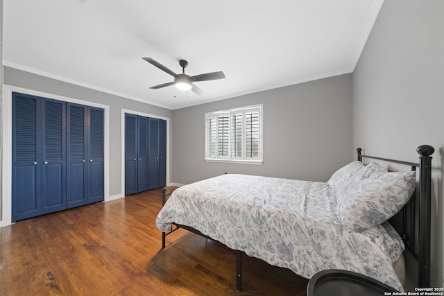 bedroom featuring ornamental molding, dark hardwood / wood-style floors, two closets, and ceiling fan