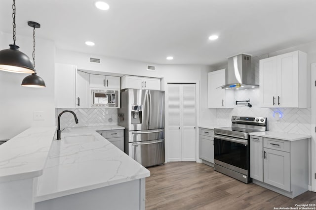 kitchen featuring sink, appliances with stainless steel finishes, white cabinetry, kitchen peninsula, and wall chimney exhaust hood