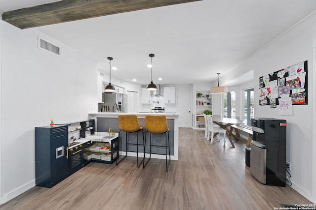 kitchen with wall chimney range hood, appliances with stainless steel finishes, a kitchen breakfast bar, white cabinets, and kitchen peninsula