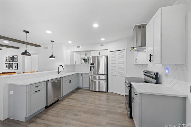 kitchen featuring pendant lighting, wall chimney range hood, gray cabinets, stainless steel appliances, and light wood-type flooring