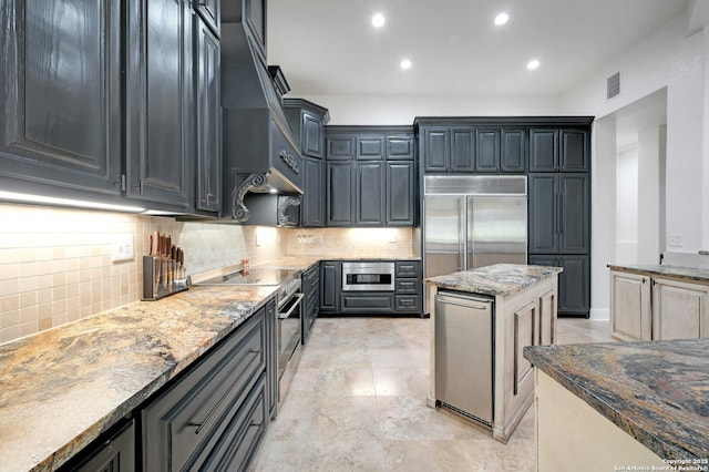 kitchen with tasteful backsplash, built in appliances, light stone countertops, and a kitchen island