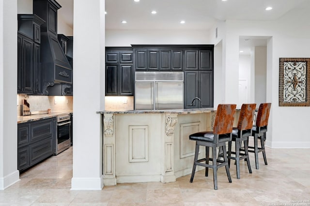 kitchen with tasteful backsplash, a breakfast bar area, stainless steel appliances, light stone countertops, and custom range hood