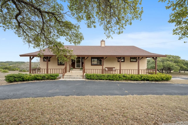 view of front of property with covered porch, a chimney, and stucco siding