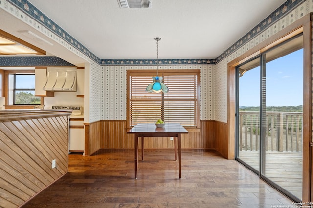 unfurnished dining area featuring wainscoting, wood finished floors, visible vents, and wallpapered walls