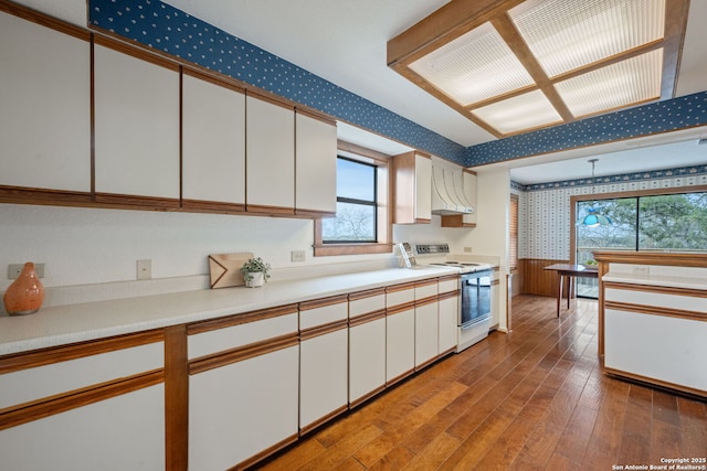 kitchen with white electric range oven, light countertops, white cabinets, wood finished floors, and wallpapered walls