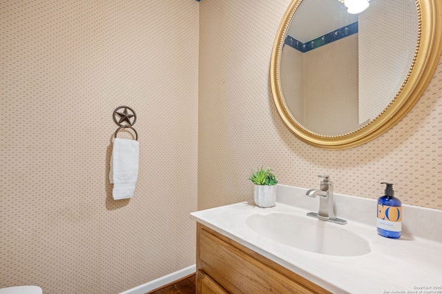 half bathroom with vanity, baseboards, and wallpapered walls